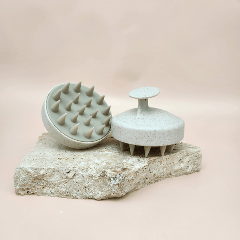 Two massage brushes showing the ergonomic handle displayed on stone with a beige background