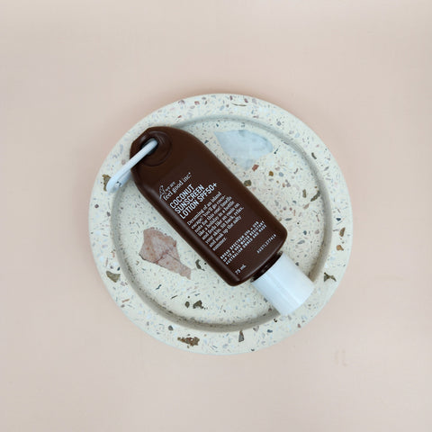 Brown bottle with white cap on a speckled ceramic plate against a pink background