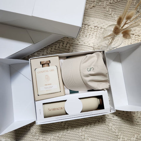 Sentimento Gifting Co. Gift set with a bottle, cap, and other items in an open box on a textured surface.